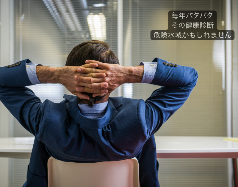 健康診断の準備に追われ、デスクで書類とパソコンに囲まれて悩む一人総務の様子